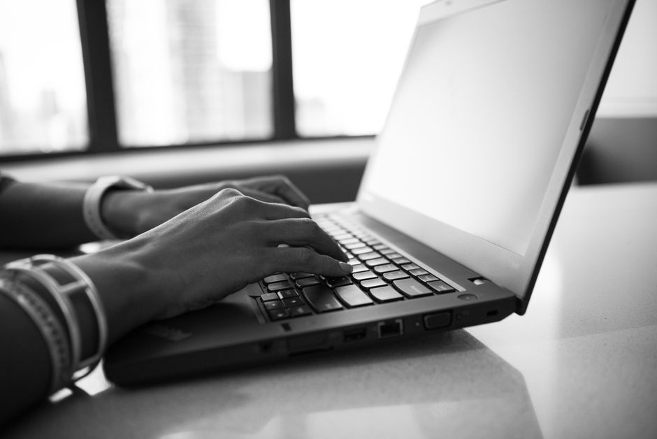 A person's hands typing on a laptop keyboard in a bright, modern office setting with blurred background