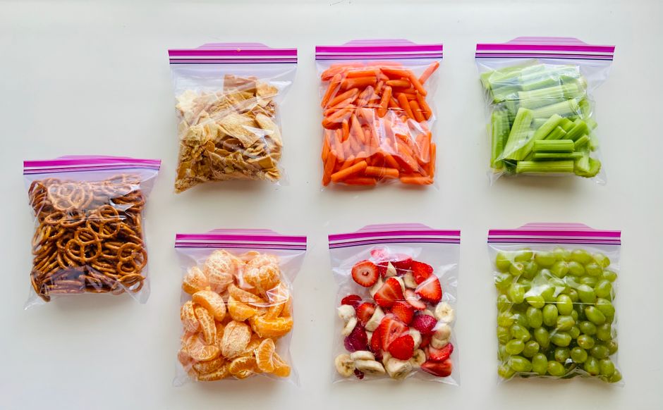 A selection of healthy snacks packed for travel, including nuts, fruit, and a water bottle, on an airplane tray table.