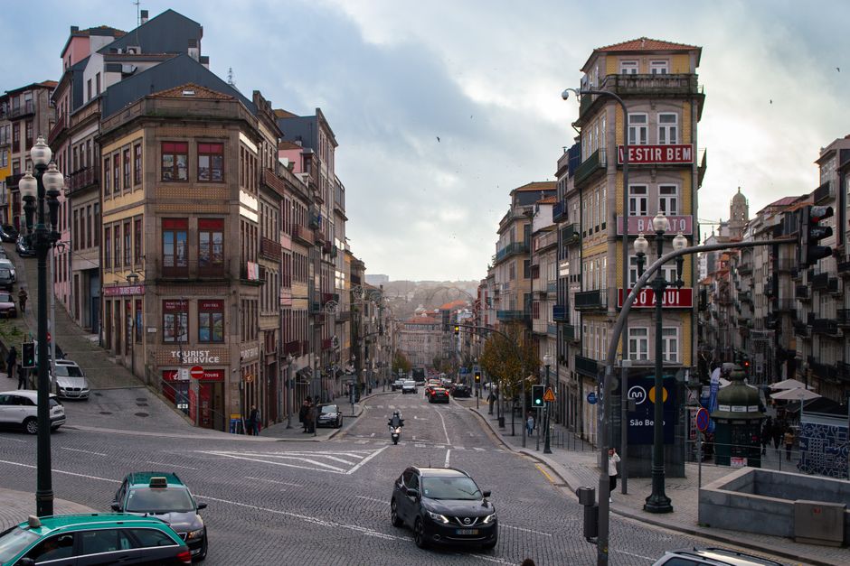 A remote worker sits at a table with a laptop, overlooking the historic Ribeira district and Douro River in Porto, Portugal.