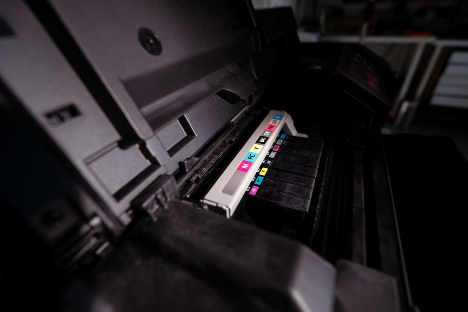 A compact ink tank all-in-one printer with large ink reservoirs visible, positioned on a clean office desk in a small business setting.