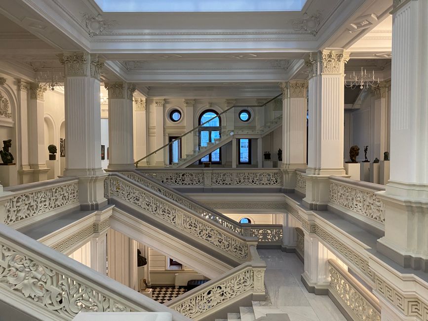The vast, ornate interior of a European art museum with several classic paintings on display.
