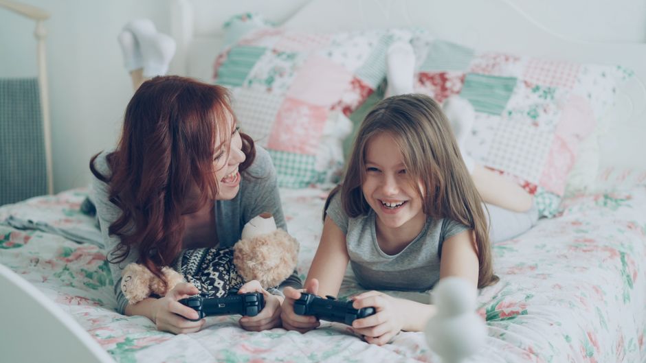 Two children and an adult sitting on a sofa, looking intently and happily at a PC monitor displaying a vibrant video game, showcasing shared family entertainment.