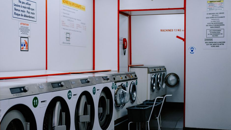 Interior view of a modern, clean self-service laundromat with rows of washing machines and dryers.