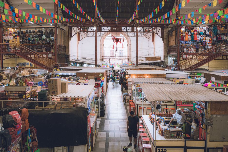 An aerial view of a vibrant local market in Mexico City, filled with colorful stalls selling fresh produce, textiles, and street food, with many people browsing.