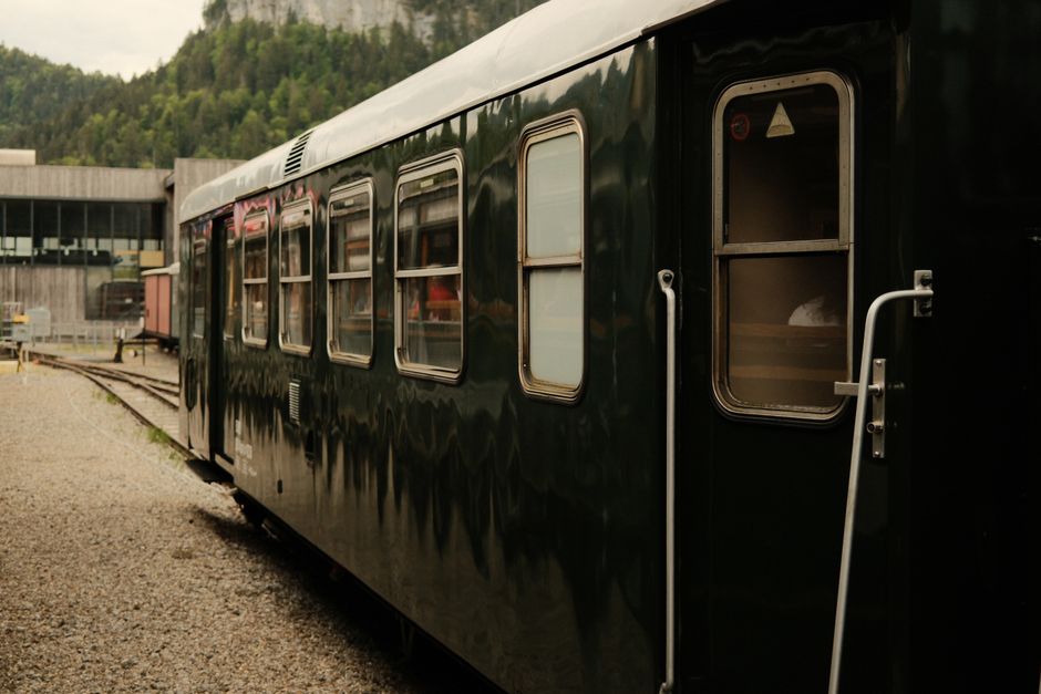 Passengers relaxing in a glass-domed observation car on a luxury train, with rugged mountains and a river visible through the windows.