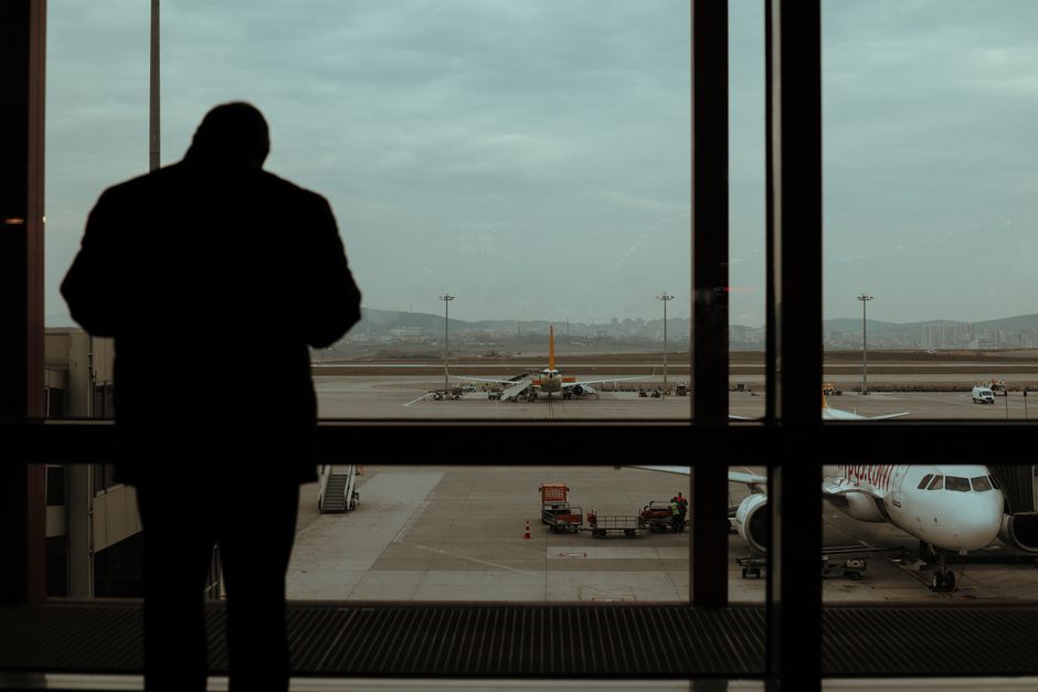 A traveler standing in an airport looking at a large digital departure board showing flights to various destinations.