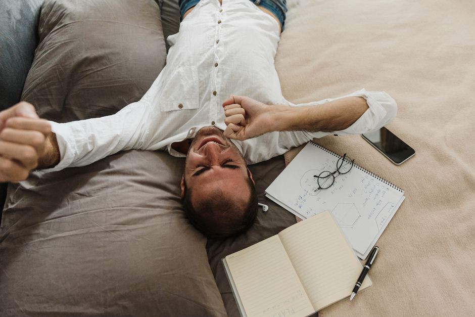 A man doing a gentle back stretch in a tight living room next to a makeshift desk, emphasizing the importance of movement in confined remote work areas.