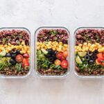 Containers filled with colorful Mediterranean-inspired meal prep components like quinoa, roasted vegetables, and chickpeas, organized on a modern kitchen counter.