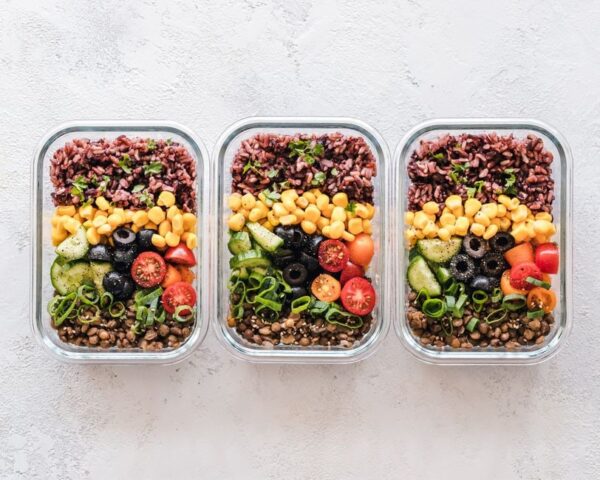 Containers filled with colorful Mediterranean-inspired meal prep components like quinoa, roasted vegetables, and chickpeas, organized on a modern kitchen counter.