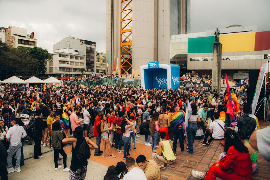 A bustling square in Medellin, Colombia, with people walking and the city's modern metro cable cars visible against green hills.