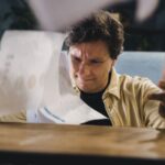 A person with a frustrated expression sitting at a chaotic desk overflowing with scattered papers and documents.