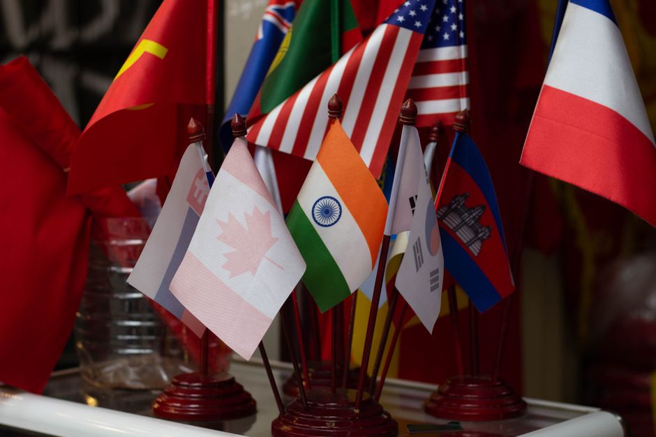 A clean, minimalist desk setup featuring a laptop, a coffee cup, and small flags representing different countries, indicating an organized, mobile lifestyle.