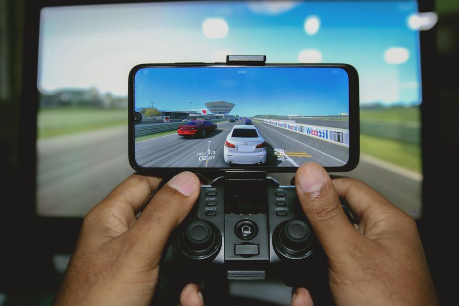 A close-up of a mobile phone screen displaying a high-fidelity cloud game being played, with a person's hands holding a Bluetooth controller, highlighting the convenience of cloud gaming for mobile users.