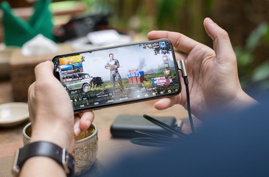 A hand holding a smartphone displaying a block-based sandbox game interface, showcasing creative building possibilities.