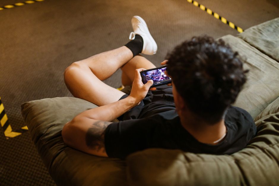 Close-up of hands holding a smartphone, playing a colorful mobile simulation game while relaxing on a comfortable sofa.