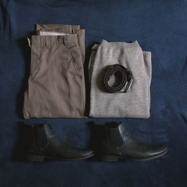 A flat lay arrangement of a capsule wardrobe featuring a trench coat, blazer, sweaters, shirts, trousers, and versatile shoes for four-season city living.