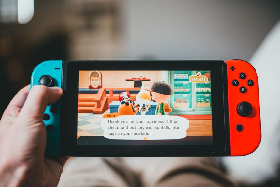 A Nintendo Switch console resting on a train table, with a blurred scenic view of mountains through the window.