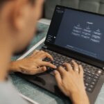 A small business owner, not a developer, looking thoughtfully at a laptop screen showing AI-generated code, with coffee on the desk.