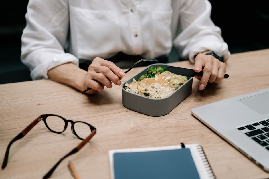 A person working at a desk with a variety of healthy snacks, including cut vegetables and fruit, neatly arranged in containers.