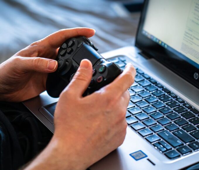 A person using an older, basic laptop to play a colorful 2D indie video game.