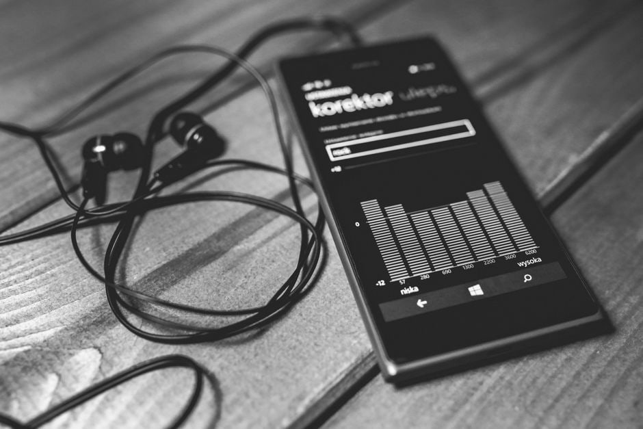 A person holding an old smartphone that is playing music through headphones, used as a dedicated media player.