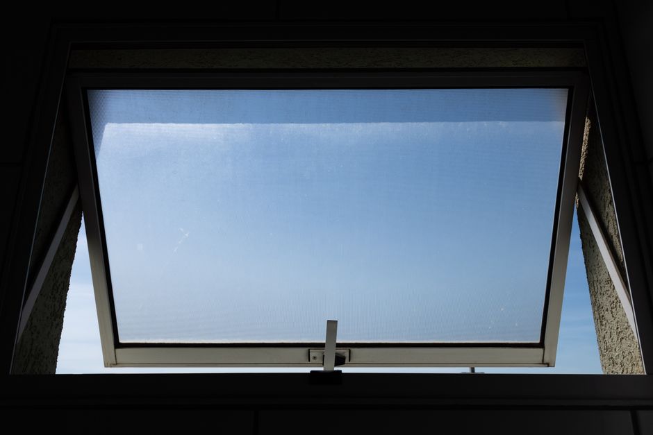 A slightly ajar window with a sheer curtain gently billowing, showing sunlight and green leaves outside, symbolizing fresh air entering a home.