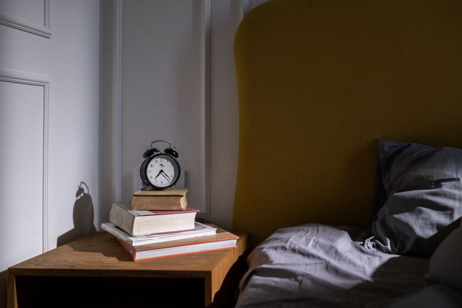 An organized nightstand featuring a traditional alarm clock, a book, and a glass of water, showing intentional avoidance of phone use in the bedroom.