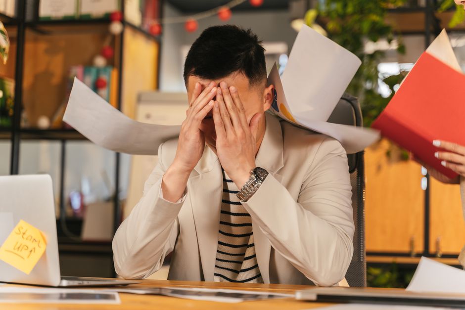 A person sitting at a desk, looking stressed and overwhelmed by a laptop screen showing an email inbox filled with hundreds of unread messages and pop-up notifications.