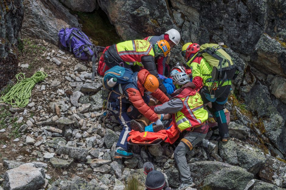 A medical team carefully moving an injured person on a stretcher through a rugged, mountainous landscape, illustrating emergency medical evacuation.