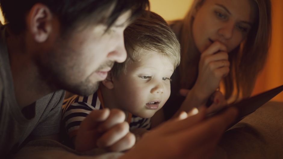 A parent and child looking at a tablet screen together, possibly reviewing settings or a game.
