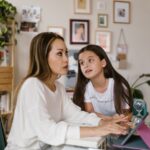 A parent and child sitting together, looking at a tablet and having a conversation about online activities.