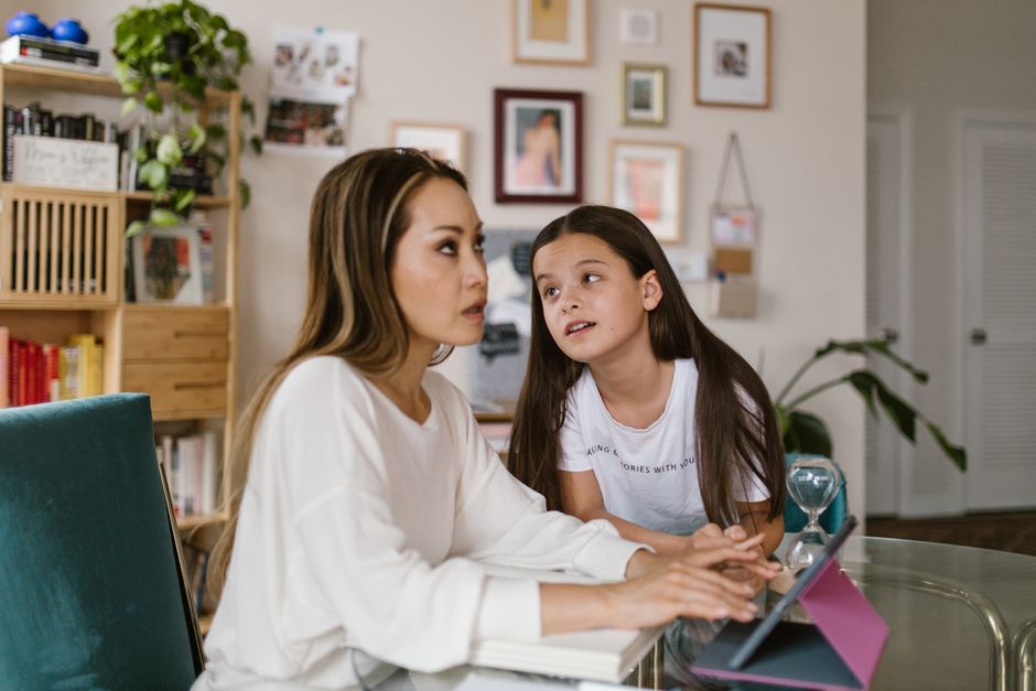 A parent and child sitting together, looking at a tablet and having a conversation about online activities.