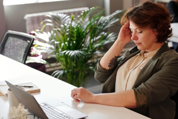 A parent with visible neck strain working at a cluttered home desk, laptop screen too low, highlighting common ergonomic mistakes.