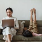 A parent sitting at a desk with a laptop, looking out a window and away from the screen, taking a mindful break from work to reduce screen fatigue.