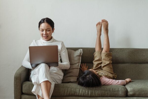 A parent sitting at a desk with a laptop, looking out a window and away from the screen, taking a mindful break from work to reduce screen fatigue.