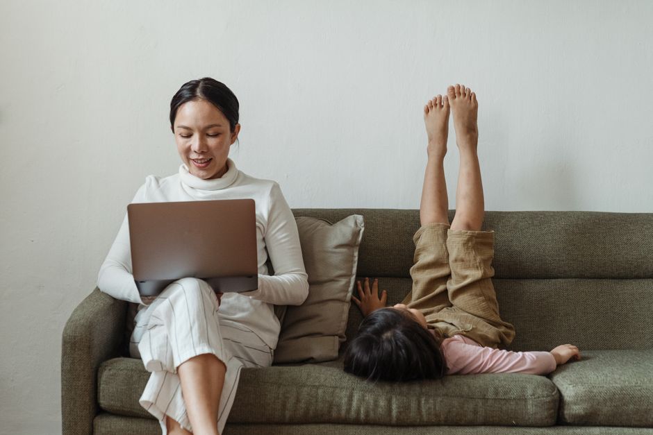 A parent sitting at a desk with a laptop, looking out a window and away from the screen, taking a mindful break from work to reduce screen fatigue.