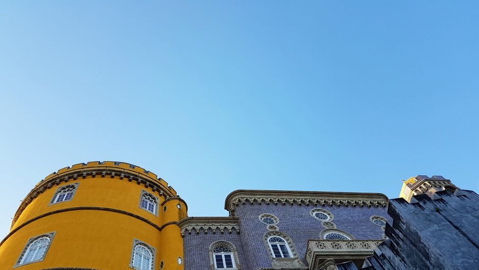 The vibrant, colorful Pena Palace in Sintra, Portugal, perched atop a hill with lush green surroundings under a bright blue sky.