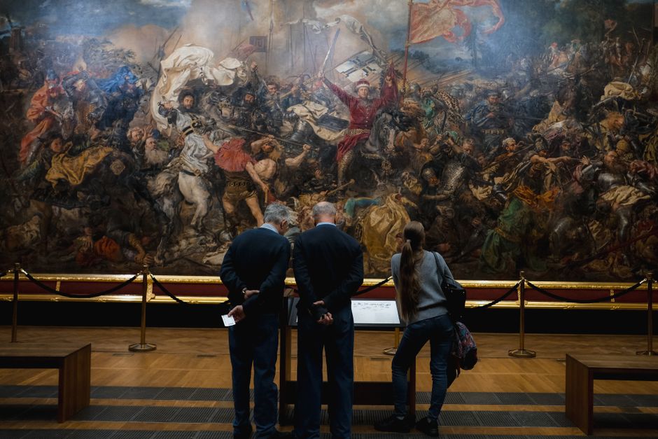 Visitors walking through a contemporary art museum, observing large abstract paintings on the walls.