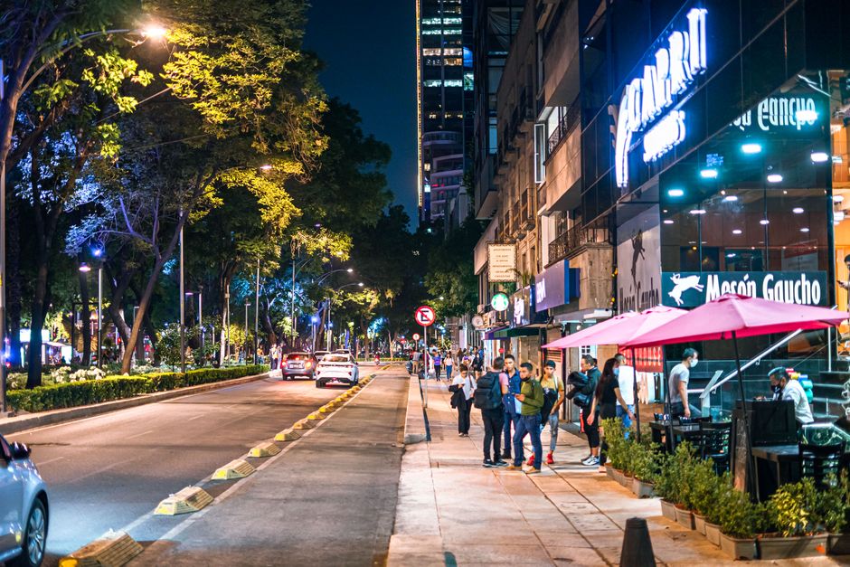 People enjoying street food and drinks at a vibrant outdoor cafe on a sunny street in Mexico City.