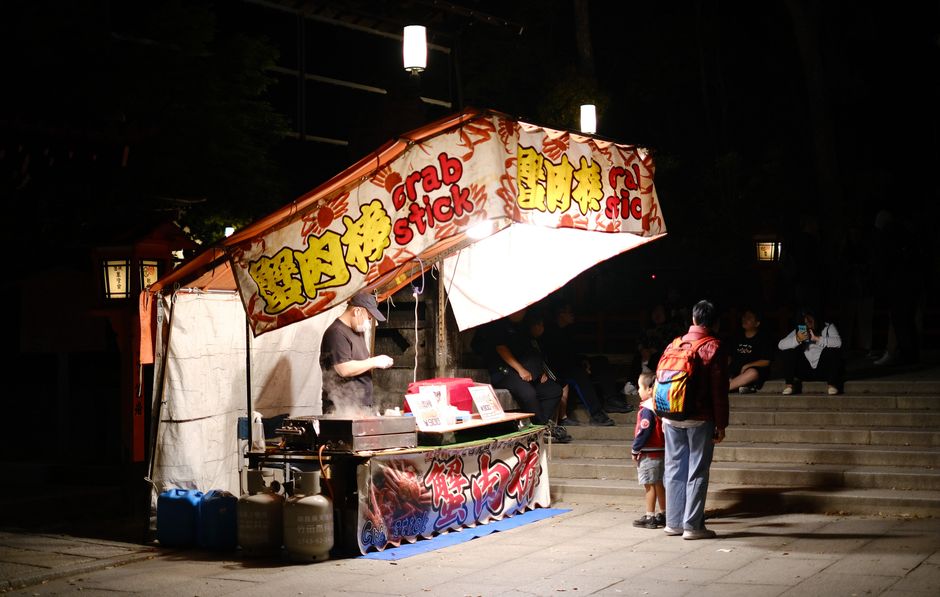 A diverse group of people enjoying various street food dishes from different vendors in a lively, well-lit street market scene, characteristic of global food travel.