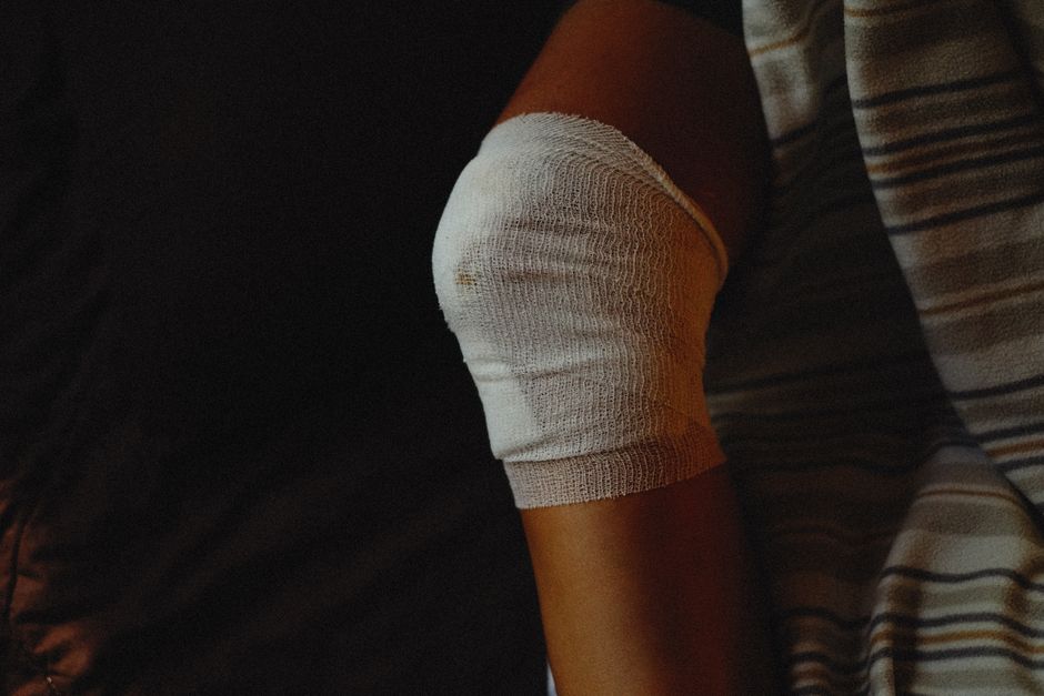A person's hand carefully applying a sterile adhesive bandage to a minor cut on their knee, demonstrating basic wound care.