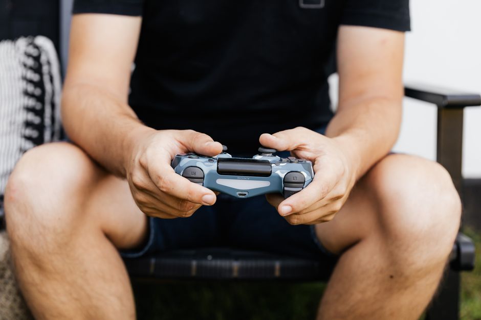 A person meticulously cleaning the crevices and joysticks of a black gaming controller with a cotton swab and cleaning solution.