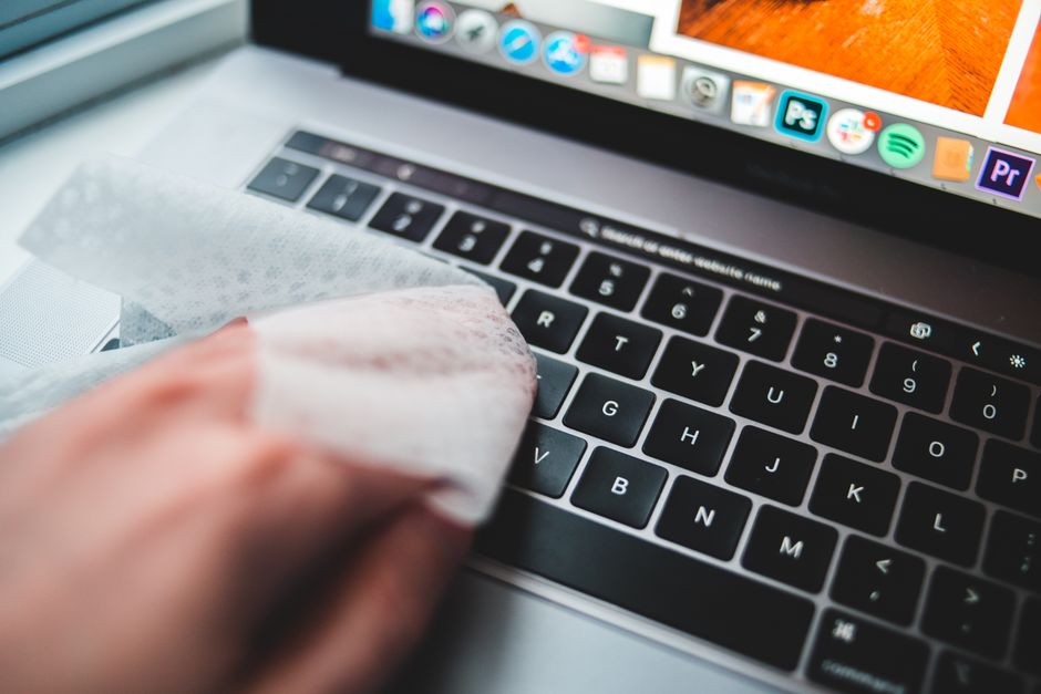 Hands gently cleaning a laptop keyboard with a small brush and compressed air, highlighting physical device maintenance.