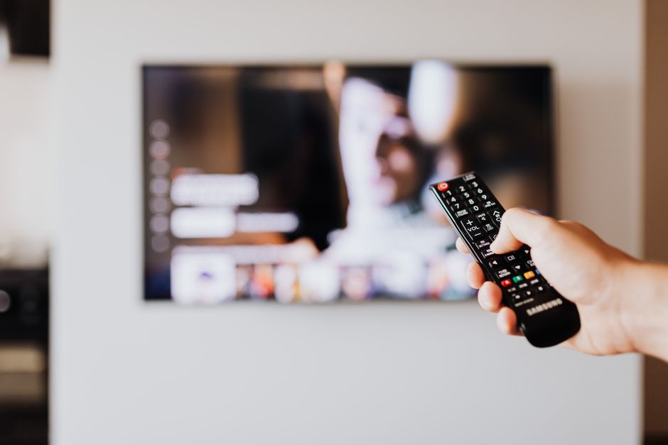 A person's hand placing a piece of tape over the small camera lens on top of a Smart TV, representing a direct action taken to ensure visual privacy and control over smart home devices.