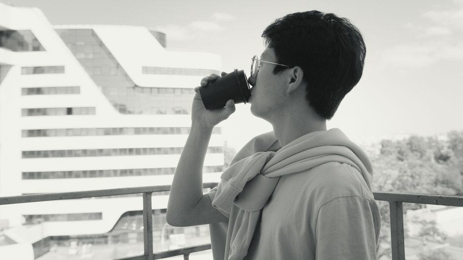 A person calmly enjoying a cup of coffee on a balcony overlooking a city skyline, emphasizing peace in an urban setting.