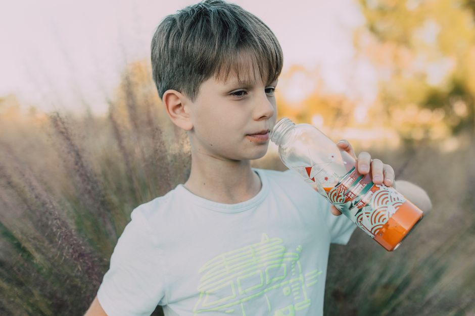 A close-up shot of a person taking a refreshing sip from a stainless steel reusable water bottle while paused against a blurred urban background.