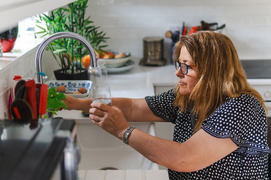 A person taking a mindful sip from a glass of water in a bright, clean kitchen, representing a healthy and proactive morning habit.