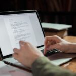 A person with headphones actively editing AI-generated text on a laptop screen, demonstrating human oversight in a creative process.
