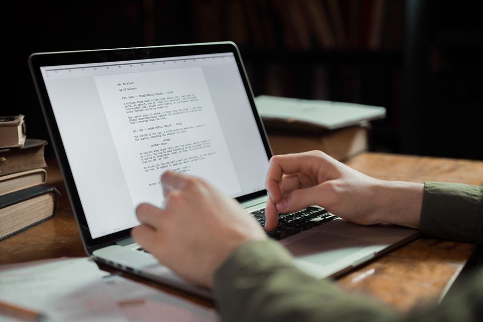 A person with headphones actively editing AI-generated text on a laptop screen, demonstrating human oversight in a creative process.