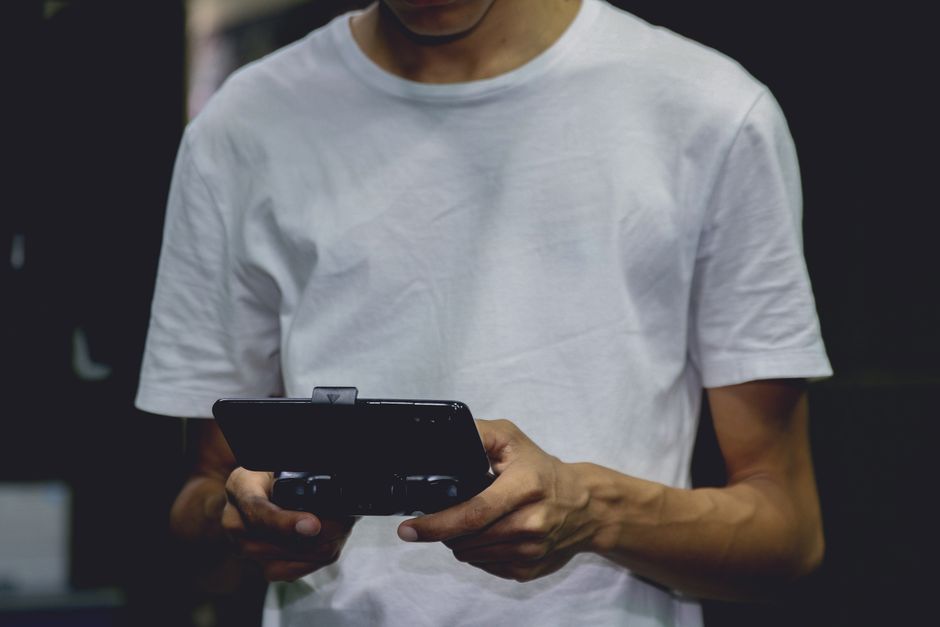 A person's hands holding a mobile gaming controller with a smartphone securely mounted in the center, playing a game.